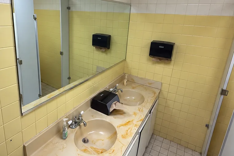 Before: dated bathroom with yellow wall tile, a worn vanity and an old mirror